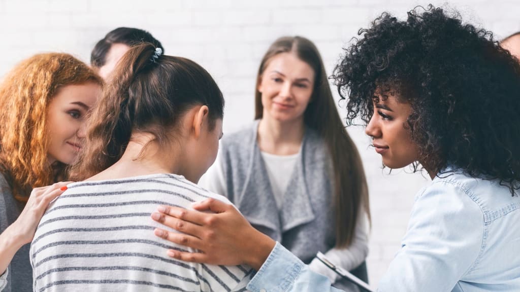 A group of women sits together indoors in Virginia, while one woman offers counseling by placing a supportive hand on another's shoulder.
